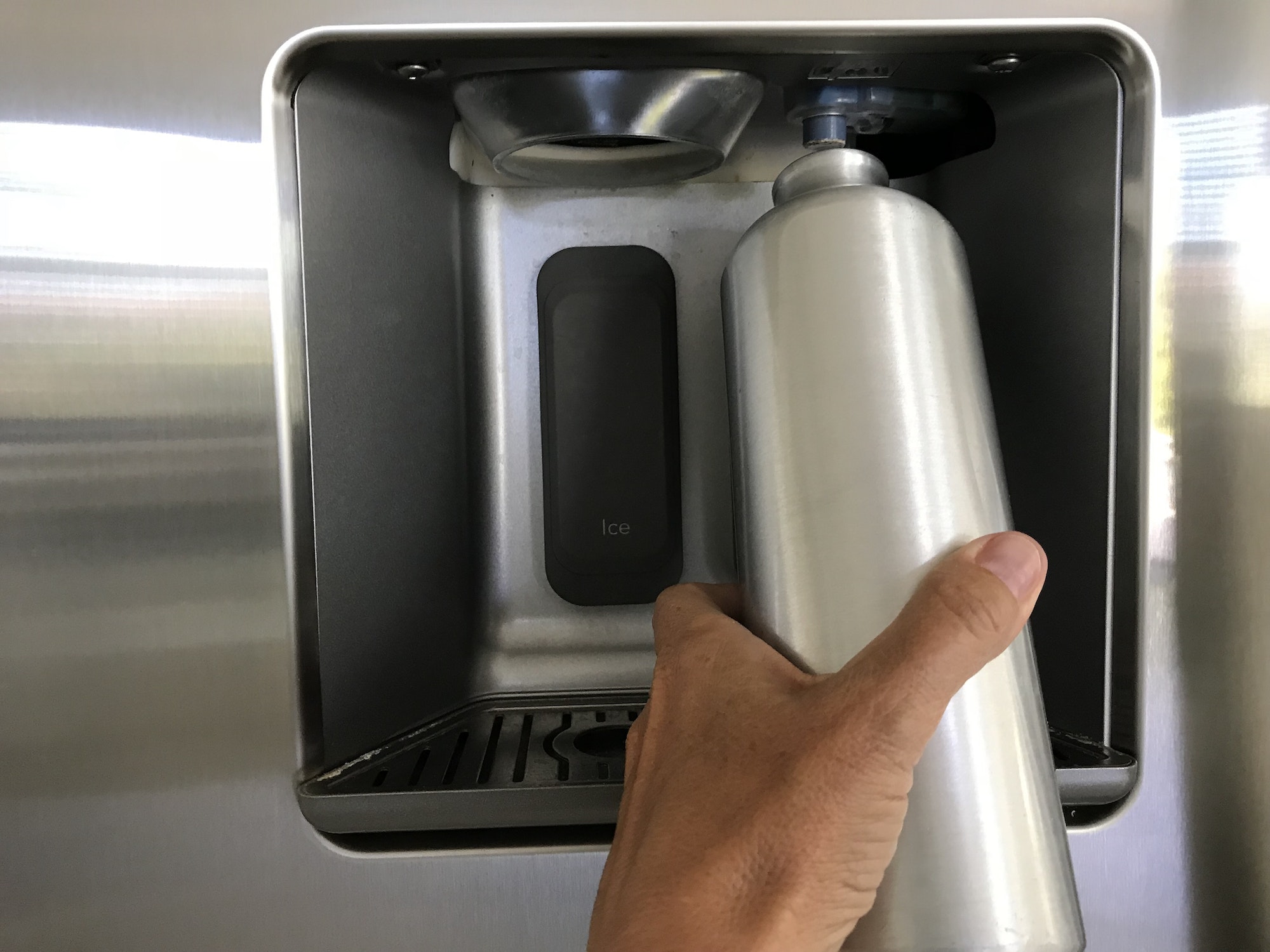A stainless steel bottle is refilled at the refrigerator with filtered water